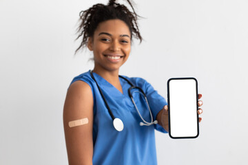 Happy black doctor showing plaster on arm and blank screen