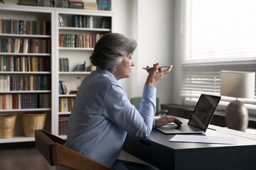 Side back view concentrated middle aged old businesswoman recording audio message on smartphone,...