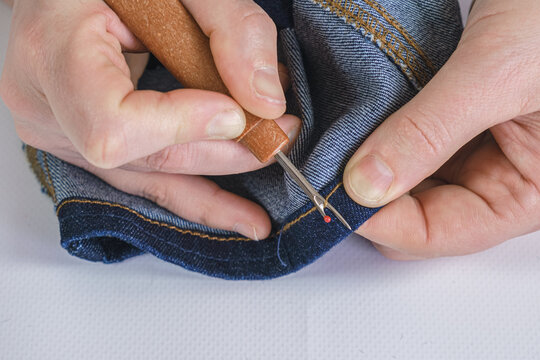 Woman seamstress rips a seam on a denim fabric with a seam ripper.