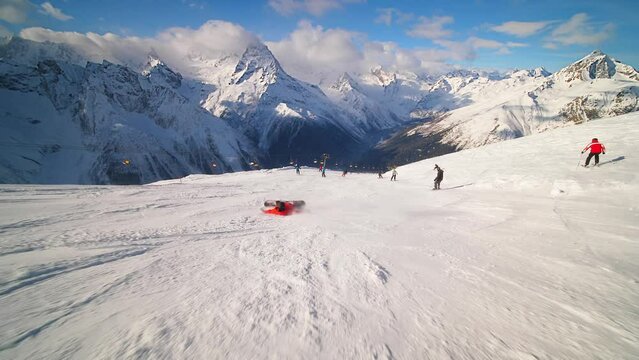 A snowboarder in an orange ski suit rolls at high speed and falls on the track
