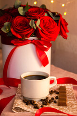 Coffee in a white cup with milk chocolate on the table against the background of red roses
