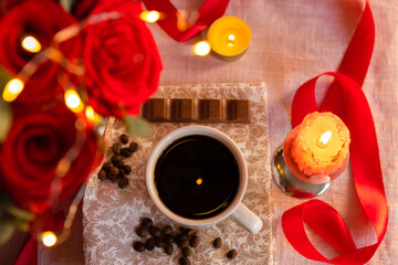 Coffee in a white cup with milk chocolate on the table against the background of red roses