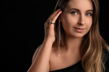 Portrait of young blonde woman with silver jewelry on black background, closeup