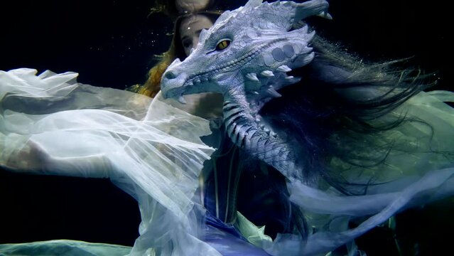 A fantastic dragon under water and his companion a woman in a long dress like in a mysterious fairy tale.