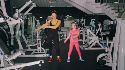 Fototapeta na wymiar Mother and daughter in the gym, family performs physical doing exercises fitness, healthy lifestyle. Happy sports family training concept. Woman with her child doing stretching warm-up in the gym