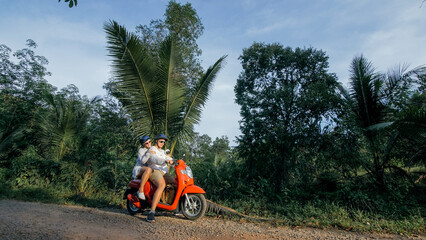 Love couple on red motorbike in white clothes to go on forest road trail trip. Two caucasian tourist woman man drive on scooter. Motorcycle rent, safety helmet, sunglasses. Asia Thailand ride tourism.
