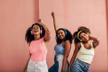 Three women having fun and dancing while listening to music with headphones