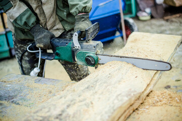 Saws in hand fitter. The man saws a thick piece of wood. From th
