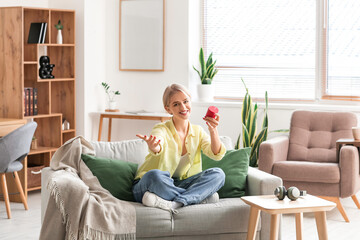 Woman sitting on sofa with wireless portable speaker and enjoying music