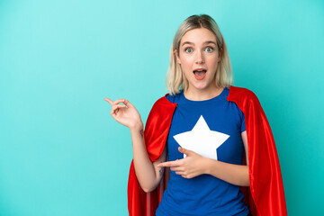 Super Hero caucasian woman isolated on blue background surprised and pointing side