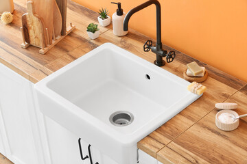 Wooden counter with ceramic sink and cleaning supplies near orange wall
