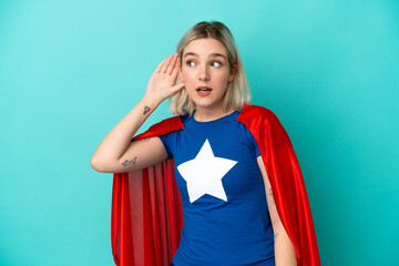 Super Hero caucasian woman isolated on blue background listening to something by putting hand on...
