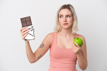 Young caucasian woman isolated on white background having doubts while taking a chocolate tablet in...