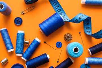 Thread spools with buttons and measuring tape on orange background