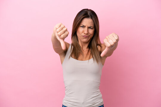 Middle age caucasian woman isolated on pink background showing thumb down with two hands