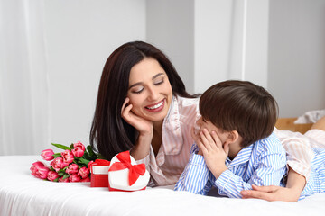 Little son and his mother with gifts and bouquet of flowers for International Women's day in bedroom at home