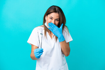 Middle age doctor woman isolated on blue background happy and smiling covering mouth with hand