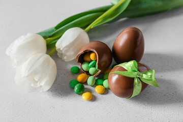 Chocolate Easter eggs with candies and tulips on light background