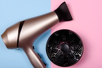 Golden hair dryer on pink and blue paper background, copy space. Top view, flat lay