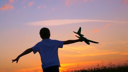 A boy at sunset runs across the field in his hands an airplane, the Kid dreams of becoming an astronaut pilot. Childhood dream to run with a toy. Pilot of a children's plane. Dream concept