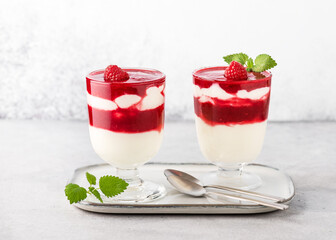 Two glasses with cold layered dessert. Raspberry sauce and buttermilk cream decorated with fresh berries and lemon balm leaves garnish. Homemade healthy sweet food concept. 