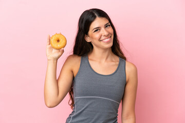Obraz na płótnie Canvas Young caucasian woman isolated on pink background holding a donut and happy