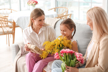 Young woman, her little daughter and mother with flowers at home on International Women's Day