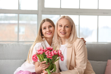 Young woman greeting her mother with bouquet of tulips at home on holiday
