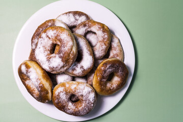 Fresh homemade donuts with white sprinkles close-up on a white plate.