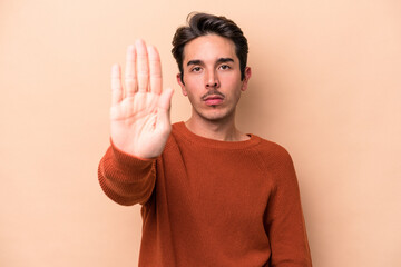 Young caucasian man isolated on beige background standing with outstretched hand showing stop sign, preventing you.