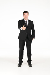 Obraz na płótnie Canvas Portrait of a smiling western business man wearing a black suit with thumbs up and his hands in his pants pocket at studio shot on white background.