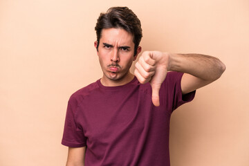 Fototapeta na wymiar Young caucasian man isolated on beige background showing thumb down and expressing dislike.