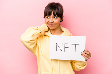 Young hispanic woman holding a NFT placard isolated on pink background touching back of head,...