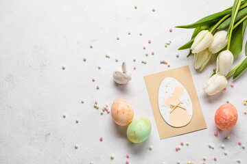 Beautiful Easter composition with greeting card, painted eggs, bunny and flowers on light background