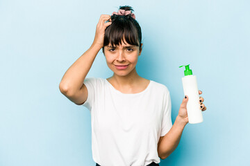 Young hispanic woman holding a body lotion isolated on blue background being shocked, she has remembered important meeting.