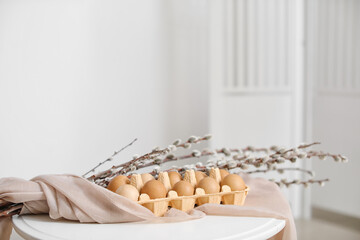 Holder with Easter eggs and pussy willow branches on table in light room
