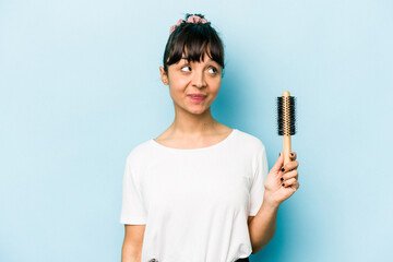 Young hispanic woman holding a brush hair isolated on blue background dreaming of achieving goals...