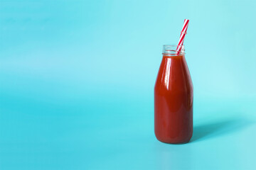 Tomato juice in a transparent bottle with a red plastic tube on a bright blue kopi space background.