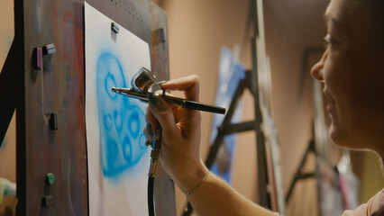Woman artist learns to paint with airbrush with acrylic dye, paper and easel. Indoors. Concept...