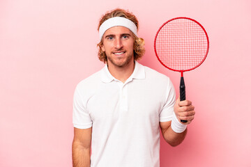 Young caucasian man playing badminton isolated on pink background happy, smiling and cheerful.