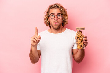 Young caucasian man holding cookies jar isolated on pink background having some great idea, concept of creativity.