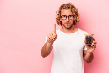 Young caucasian man holding coffee jar isolated on pink background showing number one with finger.