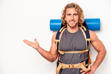 Young mountaineer caucasian man with a big backpack isolated on white background showing a copy space on a palm and holding another hand on waist.