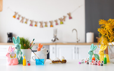 Easter decor, paints and flowers on table in kitchen