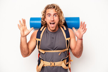 Young mountaineer caucasian man with a big backpack isolated on white background receiving a pleasant surprise, excited and raising hands.