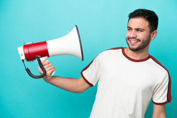 Young Brazilian man isolated on blue background holding a megaphone with stressed expression