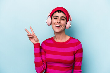 Young caucasian woman listening to music isolated on background joyful and carefree showing a peace symbol with fingers.