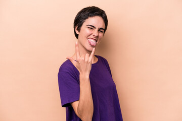 Young caucasian woman isolated on beige background showing rock gesture with fingers