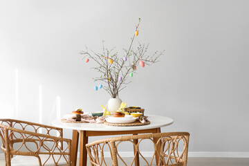 Tree branches decorated with Easter eggs on served dining table in room