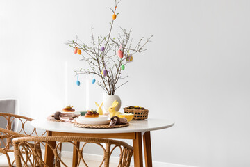 Tree branches decorated with Easter eggs on served dining table in room